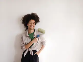 En kvinna som håller i en roller framför en beigemålad vägg