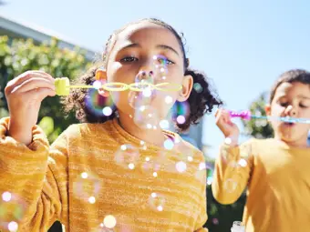 Barn i gula tröjor som blåser såpbubblor en solig dag