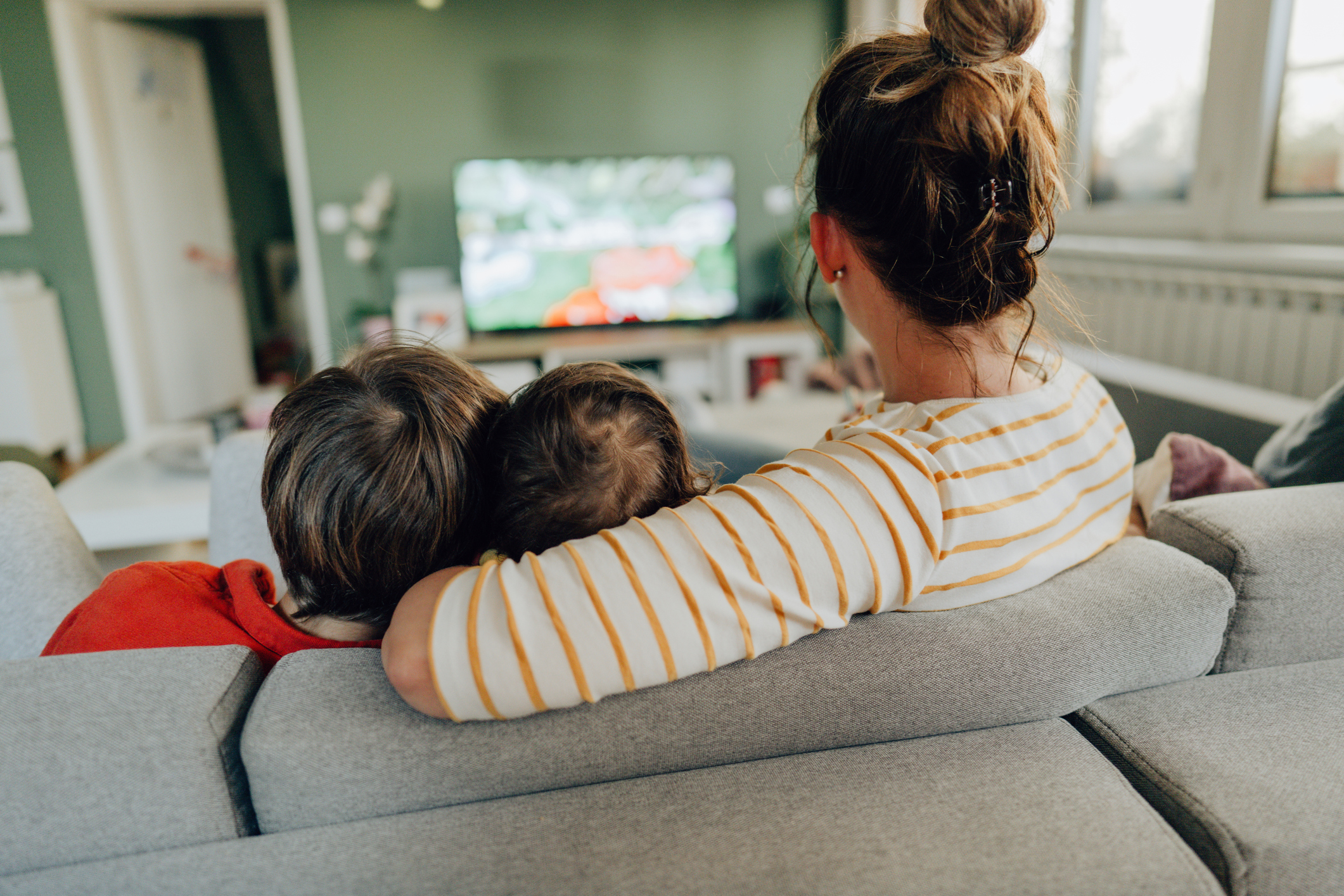 En mamma sitter med sina två barn i soffan och tittar på tv